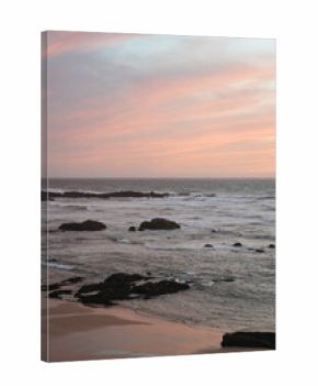 Rocky beach on the coast of Portugal. Waves, foam, pastel sky with pink and purple hues, peaceful scene, natural depth, sunset atmosphere.
