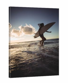 Long white surfboard leaning against gentle waves as warm sunset light sparkling on wet sand