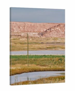 A large red potash mine tailings pile behind a small industrial building and water ponds under cloudy skies in Saskatchewan, Canada.