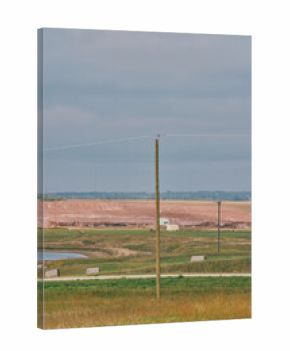 A large red potash mine tailings pile behind a small industrial building and water ponds under cloudy skies in Saskatchewan, Canada.