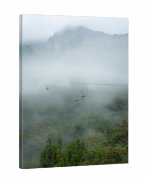 Cable cars travel through misty mountains in Yichang, China, above green forests reaching towards the sky.
