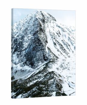 Snow-covered mountain peak with rocky slopes and a cloudy sky. The landscape showcases winter scenery and natural beauty