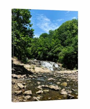 Waterfall Kinkaid Lake Spillway over rocks in Southern Illinois forest under clear blue sky