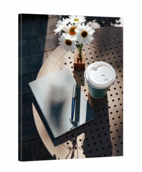 Coffee and notebook on a sunny table with flowers during a peaceful afternoon