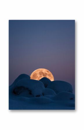 Full Moon rising over winter landscape with snow covered rocks.