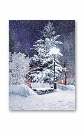 Winter city park with Christmas mood, a bench covered with snow in the night park among frosty winter trees and street shining lanterns. Festive winter night landscape of city park under falling snow