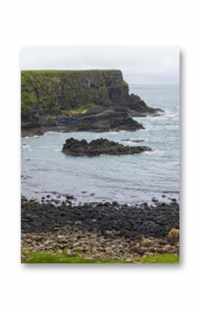 Vertical view of Bay of the Cow near Giant Causeway, Northern Ireland, showing layered earth, rocky shore, and towering basalt cliffs