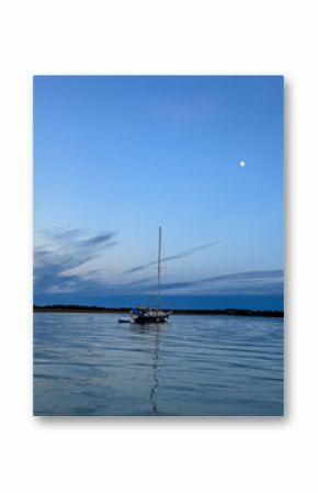 Peaceful sailboat anchored in calm coastal waters at dusk with a full moon rising over Wild Dunes, Charleston, SC. A tranquil nautical scene capturing stillness, beauty, and evening light.