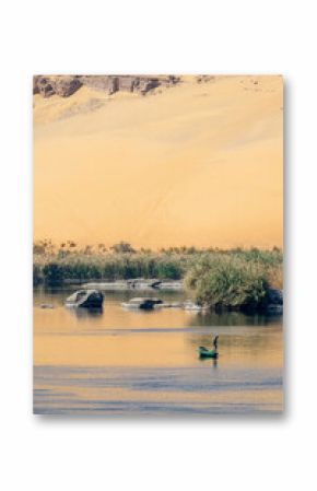 Fisherman in a rowboat on the Nile river at sunet, scenic landscape with rocks in the water and sand dune reflections in Aswan, Egypt