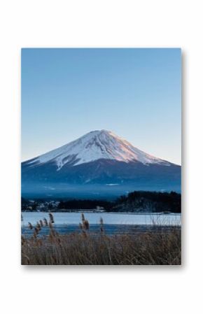 A majestic snow-capped fuji mountain rises majestically above a tranquil lake, its peak piercing the clear blue sky.