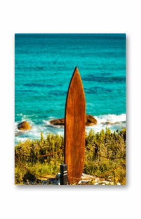 Rustic surfboard sculpture overlooking the turquoise ocean with coastal vegetation 