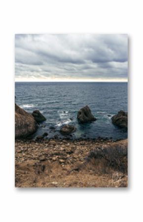 Rocky coastline under a cloudy sky with ocean waves crashing against the shore at dusk