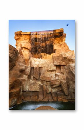 Majestic waterfall cascading over rocky cliffs at sunset with clear blue sky and serene water below