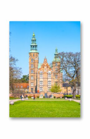 Visitors stroll through the gardens of Rosenborg Castle, a stunning renaissance structure in Copenhagen, Denmark. The clear blue sky enhances the beauty of the historic architecture.