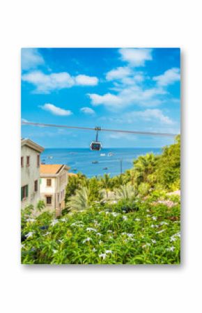 Tropical coastal view with flowering plants, seaside buildings and a cable car gondola moving over the ocean on Phu Quoc island, Vietnam at Sunset town with Mediterranean style architecture