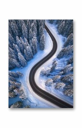 Curvy road in snow covered forest, top down aerial view
