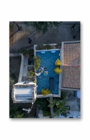 Aerial view of a cozy rooftop terrace where a woman relaxes with a white dog and lemonade. Surrounded by plants and blue tiles, the space evokes calm urban living and pet companionship