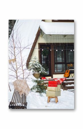 A frame triangular countryside house in the village in winter. Snowy sunny day, Christmas festive decorations outdoor. Cozy fireplace outside