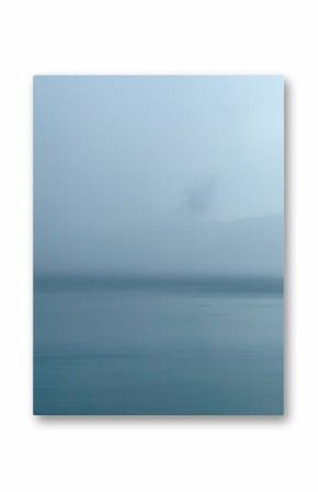 Misty seascape on a foggy day. Calm water and sky blending on the horizon. Minimalist and atmospheric nature background.