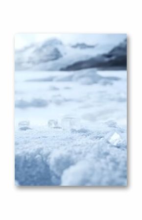 Transparent ice cubes scattered on fresh snow surface with blurred winter mountain landscape background, creating minimalist cold atmosphere composition.