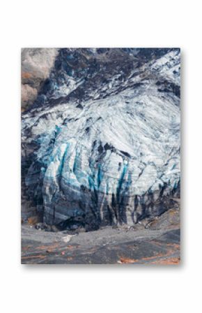 A glacier in Iceland features vivid blue ice streaks and dark crevices, surrounded by rocky terrain with orange vegetation and intricate ice patterns.