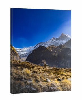 Himalayan mountain valley with snow peaks of my. Fishtail and blue sky. Dyr grassland meadows and a stone house.