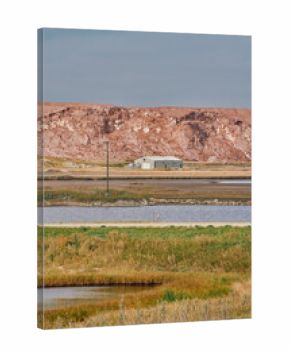A large red potash mine tailings pile behind a small industrial building and water ponds under cloudy skies in Saskatchewan, Canada.