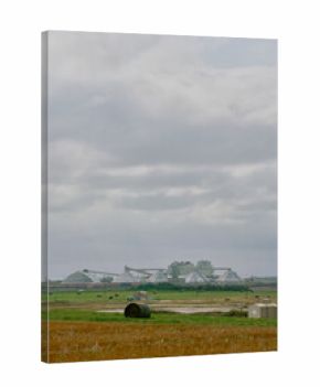 Wide view of a potash mining facility in Saskatchewan, Canada, featuring domed storage buildings, factory structures, red tailings pile, and cloudy prairie landscape in the foreground.