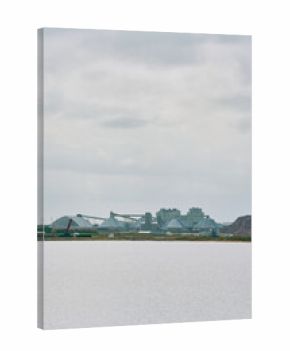 Industrial potash facility with dome storage buildings and conveyor systems viewed across a body of water in Saskatchewan, Canada, under a dramatic cloudy sky.