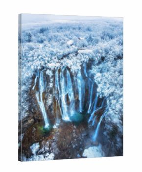 Aerial drone view of amazing waterfall and snowy forest at sunset. Winter fairytale in Plitvice Lakes, Croatia. Top view of white snow-covered frozen trees, waterfall, house, clouds on cold winter day