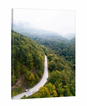 Aerial view of a winding mountain road surrounded by dense autumn forest covered with mist and fog