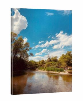 Peaceful river landscape with lush green trees, blue sky, and white fluffy clouds reflecting on calm water surface, serene nature scene in springtime countryside, natural outdoor tranquility.