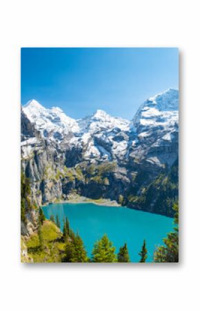 Oeschinensee lake with snow Bluemlisalp mountain on sunny summer day. Panorama of the azure lake Oeschinensee, pine forest in Swiss alps, Kandersteg. Switzerland.