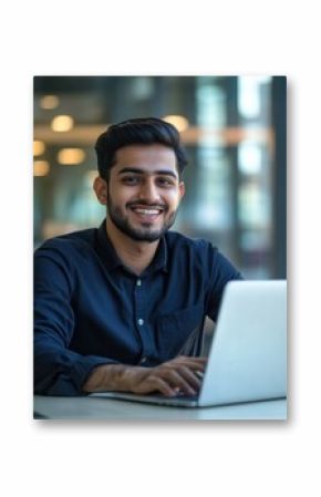 Smiling indian businessman working on laptop in modern office lobby space. Young indian student using computer remote studying, watching online webinar, zoom virtual training on video call meeting.