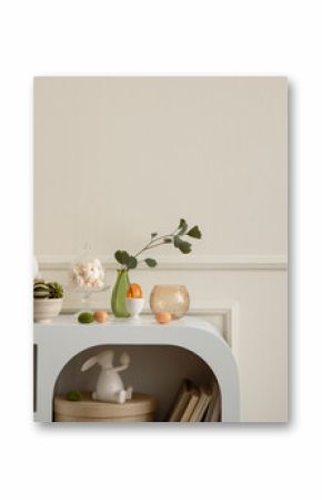 Minimalist composition of easter living room interior with copy space, easter bunny sculpture, easter eggs, vase with dried flowers, wall with stucco and personal accessories. Home decor. Template.