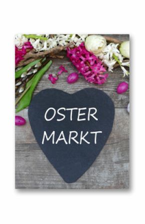 Der Text Ostermarkt auf ein Herz geschrieben mit Osterdekoration und Blumen.