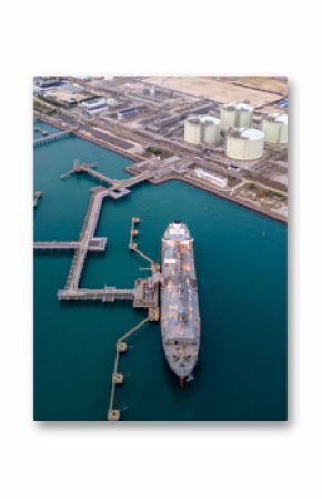 Aerial view of an LNG tanker docked at an offshore terminal with multiple pipelines, storage tanks, and an industrial complex. Captures global energy logistics
