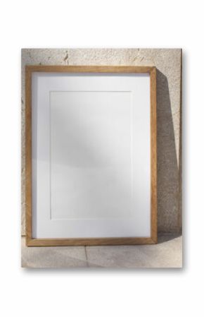 Vertical wooden picture frame leaning against stone wall in sunlight. Textured beige tiles background. Summer outdoor natural, minimal backdrop. Empty poster mockup, branding display.