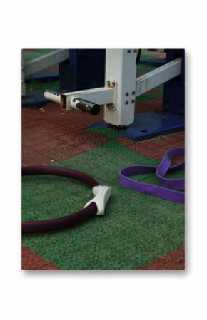 Gym equipment objects in outdoor urban street sport ground with safe rubber surface green red colors. Pilates ring, fitness band lying on the floor with no people. Closeup