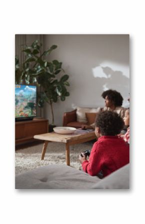 A loving family, including kids, joyfully play video games together on a TV in their cozy living room. A warm, modern scene showcasing leisure and connection.