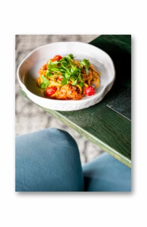 Top view of a bowl with noodles, cherry tomatoes, and cilantro on a rustic green table, capturing a vibrant and appetizing vegetarian meal.