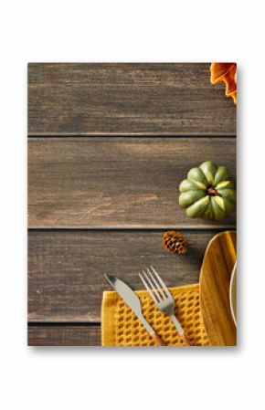 Rustic autumn table setting with empty plate, cutlery, pumpkins, nuts, and candle on wooden background. Perfect for Thanksgiving, harvest, or seasonal food themes.
