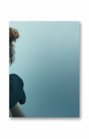[The contemplative woman seated against a soft blue backdrop in moody studio lighting]