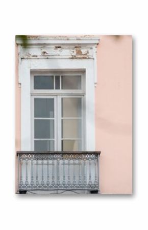 Ornate balcony with a vintage window on a pastel pink building facade, framed by blurred greenery