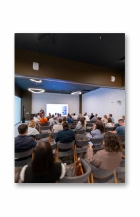People attending a professional presentation in a modern conference room with a speaker presenting on a screen.