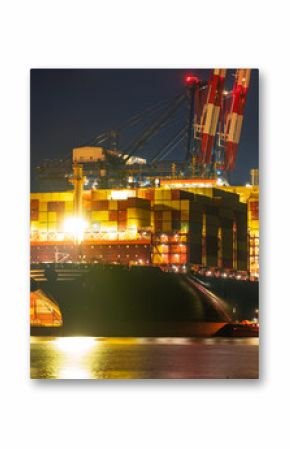 A massive container ship unloading at a container terminal in a seaport at night