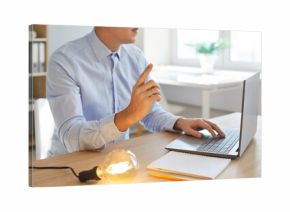 Young intelligent businessman with laptop, paper and glowing light bulb changes marketing plan using genius brain, knowledge and new smart ideas. Business creativity, technology, inspiration concept