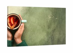 Woman's hands holding cup of hot mulled wine on green background with space for text, top view