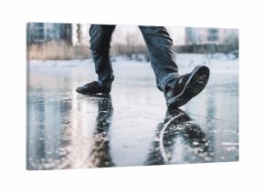 Boots standing on icy ground, illustrating the danger of slipping on a frozen, slippery winter surface. man walks cautiously along an icy street on a winter day for fear of slipping and falling.
