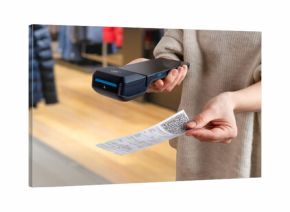 Hand offering printed receipt with QR code next to POS terminal inside clothing store, showing modern payment and checkout workflow